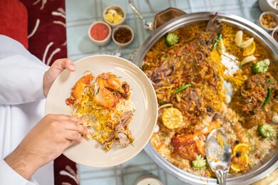 الاستمتاع بالغداء في الخارج, حسن الكرم والضيافة , مطاعم و كافيهات الامارات, صورة مقربة ليد رجلان عربيان خليجيان إماراتيان يرتديان الكندورة والغترة، يجلسان على مائدة مليئة بالمأكولات الشرقية اللذيذة ويتشاركان الطعام, إيماءات السعادة و السرور