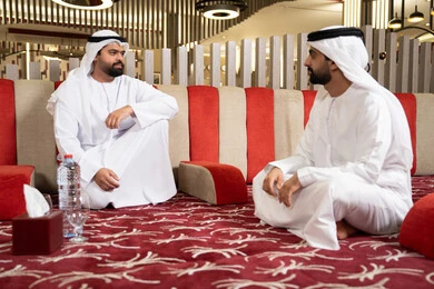 إيماءات البشاشة والترحيب، الكرم والضيافة عند العرب، صب القهوة من الدلة النحاسية، مجموعة اصدقاء عرب خليجيون اماراتيون يرتدون الكندورة والغترة فى رحلة تخييم برية، كشتة بر عربية شعبية، قضاء أوقات ممتعة مع الأصدقاء