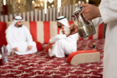 مجموعة اصدقاء عرب خليجيون اماراتيون يرتدون الكندورة والغترة فى رحلة تخييم برية، إيماءات البشاشة والترحيب، الكرم والضيافة عند العرب، صب القهوة من الدلة النحاسية،كشتة بر عربية شعبية، قضاء أوقات ممتعة مع الأصدقاء