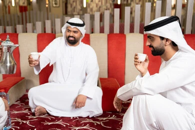 قضاء أوقات ممتعة مع الأصدقاء، إيماءات البشاشة والترحيب، الكرم والضيافة عند العرب، صب القهوة من الدلة النحاسية، مجموعة اصدقاء عرب خليجيون اماراتيون يرتدون الكندورة والغترة فى رحلة تخييم برية، كشتة بر عربية شعبية