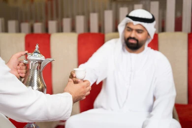 صب القهوة من الدلة النحاسية، إيماءات البشاشة والترحيب، الكرم والضيافة عند العرب، مجموعة اصدقاء عرب خليجيون اماراتيون يرتدون الكندورة والغترة فى رحلة تخييم برية، كشتة بر عربية شعبية، قضاء أوقات ممتعة مع الأصدقاء