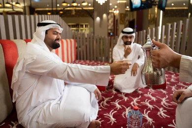 الكرم والضيافة عند العرب، إيماءات البشاشة والترحيب،صب القهوة من الدلة النحاسية، مجموعة اصدقاء عرب خليجيون اماراتيون يرتدون الكندورة والغترة فى رحلة تخييم برية، كشتة بر عربية شعبية، قضاء أوقات ممتعة مع الأصدقاء