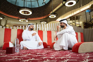 Spending enjoyable times with friends, gestures of cheerfulness and welcome, generosity and hospitality among Arabs, pouring coffee from the brass coffee pot, a group of Arab Gulf Emirati friends wearing the kandura and ghutrah on a camping trip, a popular Arab outdoor gathering.