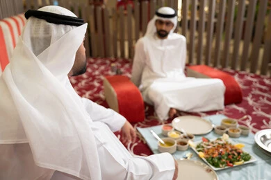 حسن الضيافة والاستقبال عند العرب ،رجلان عربيان خليجيان إماراتيان يرتديان الكندورة والغترة يجلسان معًا داخل خيمه في أجواء دافئة ويتناولان وجبة تقليدية لذيذة من الأرز والمأكولات الشرقية، مفهوم الضيافة العربية والأجواء الاجتماعية، مشاركة الطعام بروح الود والتقارب، خلفية داخلية مليئة بالتفاصيل الشرقية الجميلة. حسن الضيافة والاستقبال عند العرب ،رجلان عربيان خليجيان إماراتيان يرتديان الكندورة والغترة يجلسان معًا داخل خيمه في أجواء دافئة ويتناولان وجبة تقليدية لذيذة من الأرز والمأكولات الشرقية، مفهوم الضيافة العربية والأجواء الاجتماعية، مشاركة الطعام بروح الود والتقارب، خلفية داخلية مليئة بالتفاصيل الشرقية الجميلة.