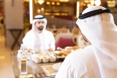 A fine restaurant in the United Arab Emirates, enjoying lunch outdoors, having a good time, restaurants and cafes in the UAE, two Arab Gulf Emirati men wearing kandura and ghutrah sharing food, gestures of happiness and joy.
