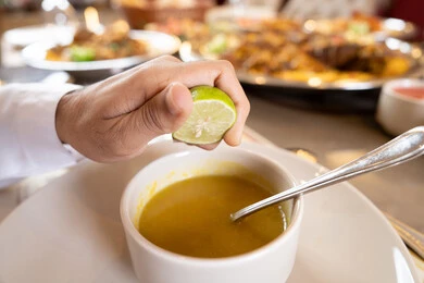 إيماءات السعادة و السرور، الاستمتاع بالغداء في الخارج, شرب المشروبات الباردة ،قضاء أوقات ممتعة في المطعم, مطاعم و كافيهات الامارات, رجل عربي خليجي اماراتي يرتدي الكندورة والغترة يجلس على المائدة و يقوم بعصر الليمون