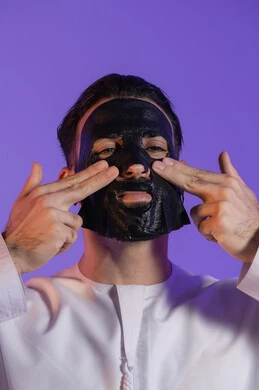 The concept of the perfect balance between purity and hydration, the power of charcoal to detoxify and purify the skin, enjoying moments of self-care, a close-up portrait of an Emirati Gulf Arab man wearing the Emirati kandura and applying a mask on his face, purple background
