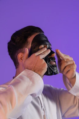 قوة الفحم في إزالة السموم و تنقية البشرة، الاستمتاع بلحظات العناية الذاتية، مفهوم التوازن المثالي بين النقاء والترطيب، بورتريه مقرب لرجل عربي خليجي اماراتي يرتدي الكندورة الاماراتية و يقوم بوضع ماسك على وجهه, خلفية بنفسجية