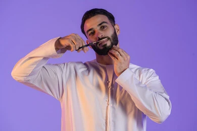 Maintaining personal hygiene, trimming and styling the beard and mustache, a men's beauty center, the concept of care and attention to beauty and appearance, a portrait of an Emirati Gulf Arab man wearing the Emirati kandura and holding scissors, purple background