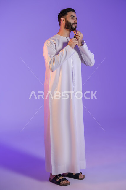استخدام أدوات و معدات الحلاقة, قص و تصفيف الذقن والشارب, مركز تجميلي رجالي، مفهوم العناية و الاهتمام بالجمال والمظهر الخارجي، بورتريه لرجل عربي خليجي اماراتي يرتدي الكندورة الاماراتية و يمسك المقص, خلفية بنفسجية