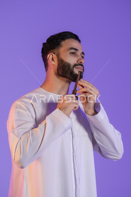 تعابير الاعجاب بالنفس، قص و تصفيف الذقن والشارب, مركز تجميلي رجالي، مفهوم العناية و الاهتمام بالجمال والمظهر الخارجي، بورتريه لرجل عربي خليجي اماراتي يرتدي الكندورة الاماراتية و يمسك المقص, خلفية بنفسجية