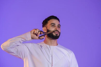 استخدام المقص في العناية الشخصية, مركز تجميلي رجالي، مفهوم  الاهتمام بالجمال والمظهر الخارجي، قص و تصفيف الذقن والشارب، بورتريه لرجل عربي خليجي اماراتي يرتدي الكندورة الاماراتية, خلفية بنفسجية