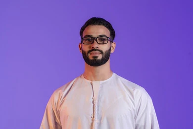 Feeling happy and joyful with clear vision, using glasses to correct vision, portrait of an Emirati Gulf Arab man wearing the Emirati kandura and wearing glasses, purple background
