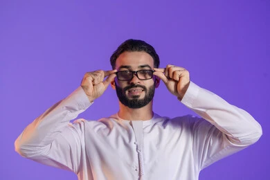 The concept of improving vision and trying to correct eyesight, taking care of one's appearance, wearing glasses for weak eyesight, a close-up portrait of an Emirati Gulf Arab man wearing the Emirati kandura and wearing medical glasses, purple background