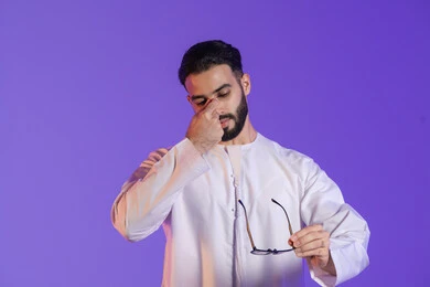 Signs of illness, migraine pain, headache and dizziness, need for treatment and rest, portrait of an Emirati Gulf Arab man wearing the Emirati kandura and holding glasses, purple background