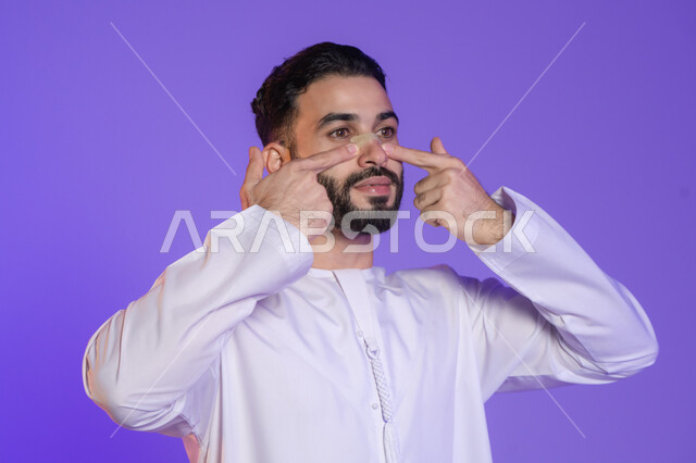 ماسك فعال لامتصاص الزيوت الزائدة, منتجات تجميلية فعالة وتقنيات حديثة، وعي الرجل العربي بأهمية العناية الشخصية، بورتريه مقرب لرجل عربي خليجي اماراتي يرتدي الكندورة الاماراتية و يقوم بوضع ماسك على أنفه, خلفية بنفسجية