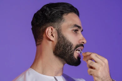 إزالة بقايا الطعام بخيط بلاستيكي, التأكد من نظافة الأسنان بعد تناول الطعام، المحافظة على ابتسامة ناصعة البياض، بورتريه لرجل عربي خليجي اماراتي يرتدي الكندورة الاماراتية و يقوم بتنظيف أسنانه,  خلفية بنفسجية