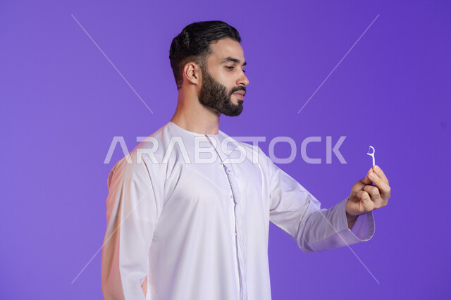 الحفاظ على نظافة الفم بخيط سني بلاستيكي, التأكد من نظافة الأسنان بعد تناول الطعام، المحافظة على ابتسامة ناصعة البياض، بورتريه لرجل عربي خليجي اماراتي يرتدي الكندورة الاماراتية و ينظر للنكاشة البلاستيكية, خلفية بنفسجية