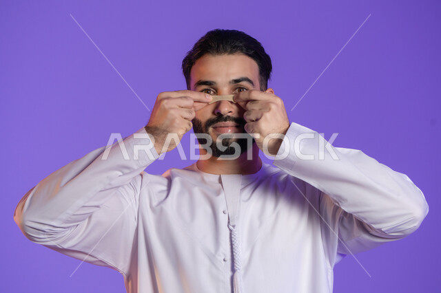 منتجات تجميلية فعالة وتقنيات حديثة، وعي الرجل العربي بأهمية العناية الشخصية، التخلص من الرؤوس السوداء والجلد الميت، بورتريه مقرب لرجل عربي خليجي اماراتي يرتدي الكندورة الاماراتية و يقوم بوضع ماسك على أنفه, خلفية بنفسجية