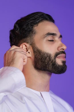 Daily ear care routine, attention to detail in personal hygiene, use of cotton swabs and sticks, portrait of an Emirati Gulf Arab man wearing the Emirati kandura and holding a cotton swab in his hand, purple background