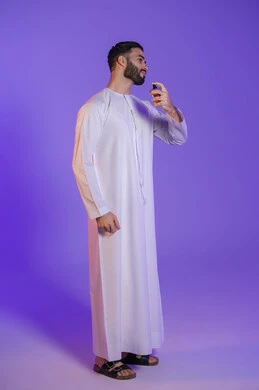 الروائح الطيبة الفواحه, استخدام الزيوت العطرية الطبيعية, مفهوم الاناقة والاهتمام بالمظهر الخارجي, التسويق لمنتجات العطور, عطورات عربيه خليجيه, بورتريه لرجل عربي خليجي اماراتي يرتدي الكندورة الاماراتية و يمسك زجاجة عطر, خلفية بنفسجية