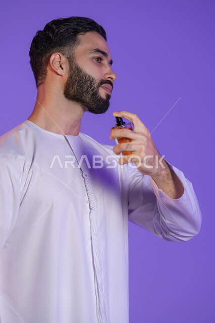 Men's grooming and decoration, use of natural aromatic oils, concept of elegance and interest in external appearance, marketing of perfume products, Arab Gulf perfumes, portrait of an Arab Gulf Emirati man wearing the Emirati kandura and holding a bottle of perfume, purple background