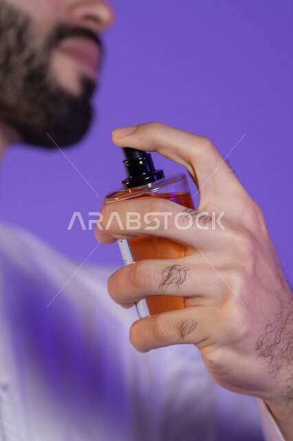Using unique scents, using natural essential oils, the concept of elegance and interest in one's appearance, marketing perfume products, a close-up portrait of a young Arab Gulf Emirati man holding a perfume bottle, purple background