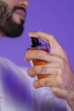 التطيب بالروائح الفريدة، استخدام الزيوت العطرية الطبيعية, مفهوم الاناقة والاهتمام بالمظهر الخارجي, التسويق لمنتجات العطور, بورتريه مقرب ليد شاب عربي خليجي اماراتي تمسك زجاجة عطر, خلفية بنفسجية
