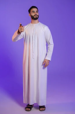 استخدام الزيوت العطرية الطبيعية, مفهوم الاناقة والاهتمام بالمظهر الخارجي, التسويق لمنتجات العطور, عطورات عربيه خليجيه, بورتريه لرجل عربي خليجي اماراتي يرتدي الكندورة الاماراتية و يمسك زجاجة عطر, خلفية بنفسجية