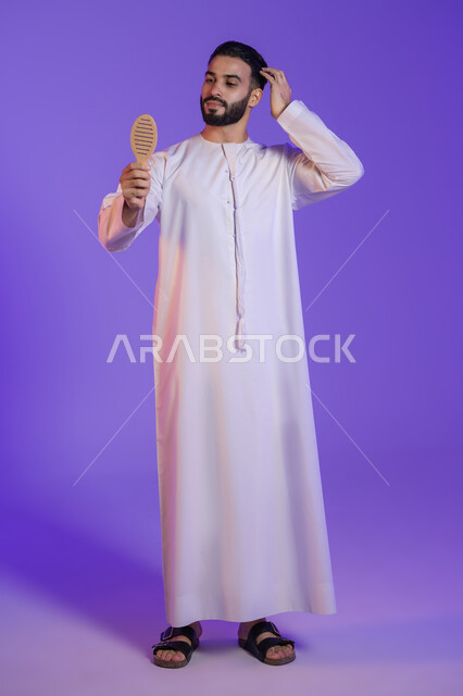 Improving the outward appearance, healthy and elegant hair, the concept of caring about beauty and elegance, a portrait of an Emirati Gulf Arab man wearing the Emirati kandura and styling his hair with a brush, purple background