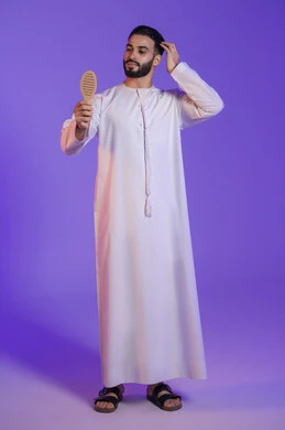 تحسين المظهر الخارجي, شعر صحي وأنيق، مفهوم الاهتمام بالجمال والأناقة، بورتريه لرجل عربي خليجي اماراتي يرتدي الكندورة الاماراتية و يقوم بتصفيف شعره باستخدام الفرشاة, خلفية بنفسجية