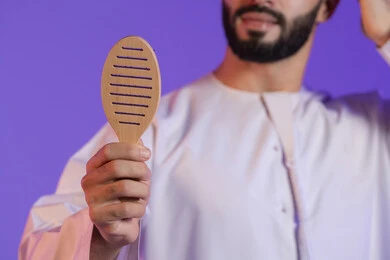 فرشاة خشبية تساعد على فك التشابك, المحافظة على شعر صحي وأنيق، مفهوم العناية والاهتمام بالجمال والأناقة والمظهر الخارجي، بورتريه مقرب ليد رجل عربي خليجي اماراتي, خلفية بنفسجية