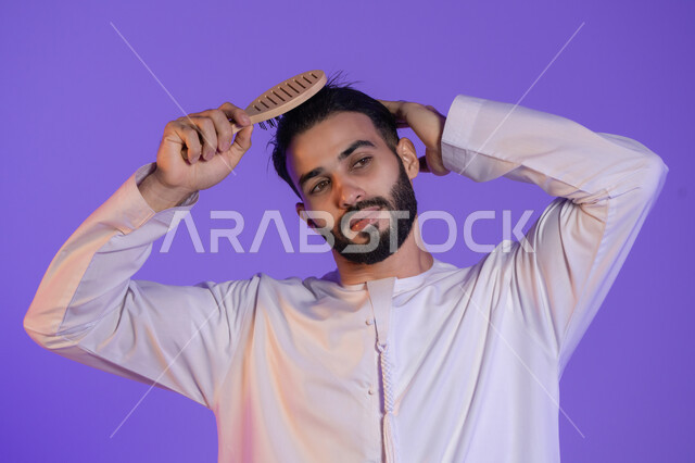 شعر صحي وأنيق، مفهوم الاهتمام بالجمال والأناقة والمظهر الخارجي،  بورتريه لرجل عربي خليجي اماراتي يرتدي الكندورة الاماراتية و يقوم بتصفيف شعره باستخدام الفرشاة, خلفية بنفسجية