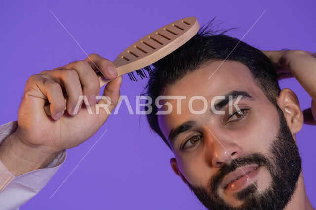 التمشيط باستخدام فرشاة الشعر، مفهوم العناية والاهتمام بالجمال والأناقة والمظهر الخارجي، بورتريه مقرب لرجل عربي خليجي اماراتي و يقوم بتصفيف شعره, خلفية بنفسجية