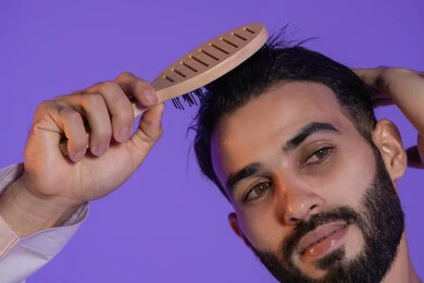 Combing with a hairbrush, the concept of care and attention to beauty, elegance and appearance, a close-up portrait of an Emirati Gulf Arab man styling his hair, purple background