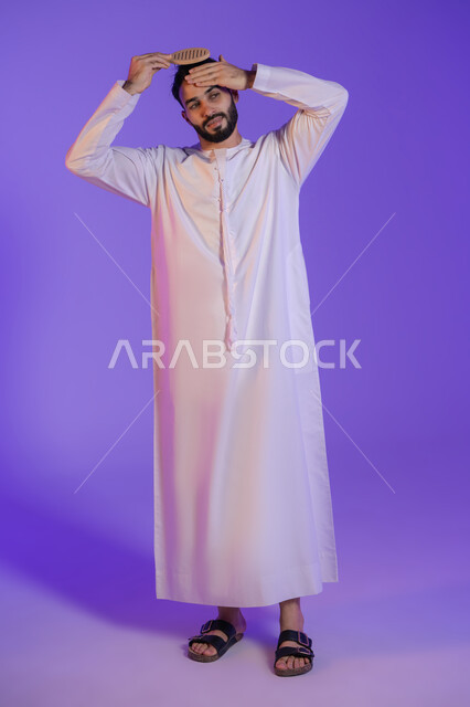 ترتيب وتمشيط الشعر، مفهوم العناية والاهتمام بالجمال والأناقة والمظهر الخارجي، بورتريه لرجل عربي خليجي اماراتي يرتدي الكندورة الاماراتية و يقوم بتصفيف شعره باستخدام الفرشاة, خلفية بنفسجية