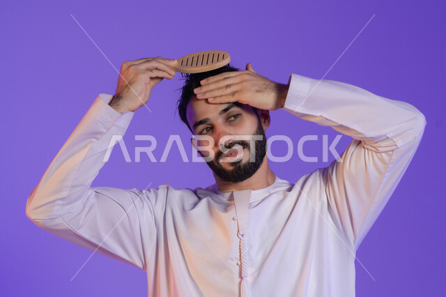 المحافظة على شعر صحي وأنيق، مفهوم الاهتمام بالجمال والأناقة والمظهر الخارجي، العناية بالنظافة الشخصية، بورتريه مقرب لرجل عربي خليجي اماراتي يرتدي الكندورة الاماراتية و يقوم بتصفيف شعره باستخدام الفرشاة, خلفية بنفسجية