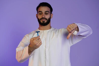 عدم الإعجاب وعدم الرضا, الحفاظ على الأناقة والنظافة الشخصية، العناية بالبشرة والاهتمام بالمظهر الخارجي، بورتريه لرجل عربي خليجي اماراتي يرتدي الكندورة الاماراتية و يمسك شفرة حلاقة, خلفية بنفسجية