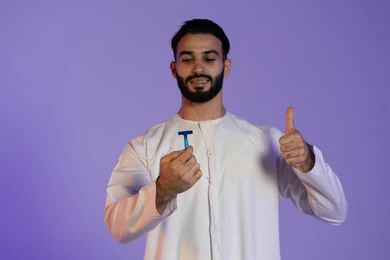 علامة التميز و الجودة, الحفاظ على الأناقة والنظافة الشخصية، العناية بالبشرة والاهتمام بالمظهر الخارجي، بورتريه لرجل عربي خليجي اماراتي يرتدي الكندورة الاماراتية يمسك شفرة حلاقة و يرفع اصبع الابهام باشارة اللايك, خلفية بنفسجية