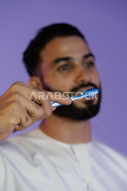Regular brushing prevents tartar buildup, freshness and health prevention, taking care of health and daily appearance, maintaining elegance and personal hygiene, maintaining a white smile, portrait of an Emirati Gulf Arab man wearing an Emirati kandura and brushing his teeth, purple background