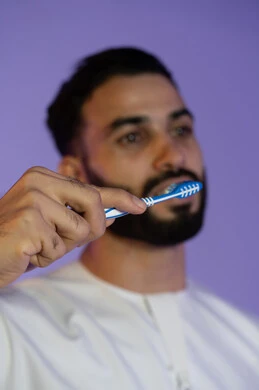 تفريش منتظم يمنع تراكم الجير, الانتعاش والوقاية الصحية, الاهتمام بالصحة والمظهر اليومي, الحفاظ على الأناقة والنظافة الشخصية، المحافظة على ابتسامة بيضاء، بورتريه لرجل عربي خليجي اماراتي يرتدي الكندورة الاماراتية و ينظف أسنانه بالفرشاة، خلفية بنفسجية