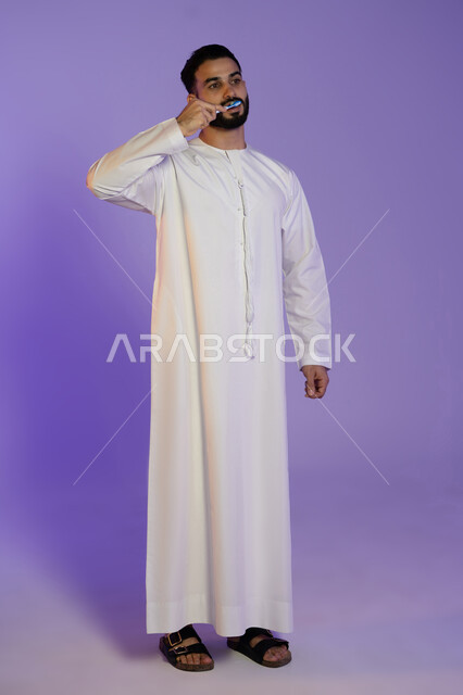 الاهتمام بالصحة والمظهر اليومي, الحفاظ على الأناقة والنظافة الشخصية، المحافظة على ابتسامة بيضاء، بورتريه لرجل عربي خليجي اماراتي يرتدي الكندورة الاماراتية و ينظف أسنانه بالفرشاة، خلفية بنفسجية
