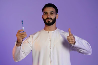 الشعور بالقبول والرضا، علامة التميز و الجودة, الحفاظ على الأناقة والنظافة الشخصية، العناية بالبشرة والاهتمام بالمظهر الخارجي، بورتريه لرجل عربي خليجي اماراتي يرتدي الكندورة الاماراتية يمسك الفرشاة يرفع اصبع الابهام باشارة اللايك، خلفية بنفسجية