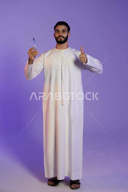 حركة يدين تدل على الاعجاب, علامة التميز و الجودة, الحفاظ على الأناقة والنظافة الشخصية، العناية بالبشرة والاهتمام بالمظهر الخارجي، بورتريه لرجل عربي خليجي اماراتي يرتدي الكندورة الاماراتية يمسك الفرشاة يرفع اصبع الابهام باشارة اللايك، خلفية بنفسجية