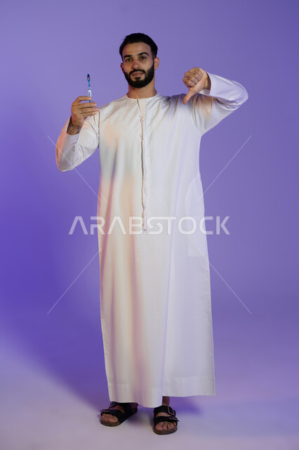 الإشاره بأصبع الإبهام لأسفل, الشعور بالإنزعاج والغضب، حماية السن من التسوس، مفهوم العناية بصحة ونظافة الفم، بورتريه لرجل عربي خليجي اماراتي يرتدي الكندورة الاماراتية يمسك فرشاة الأسنان, خلفية بنفسجية