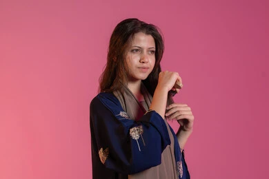 Healthy and tidy hair, interest in beauty and elegance, personal hygiene, portrait of an Emirati Gulf Arab woman wearing a blue abaya and combing her hair with a brush, pink background