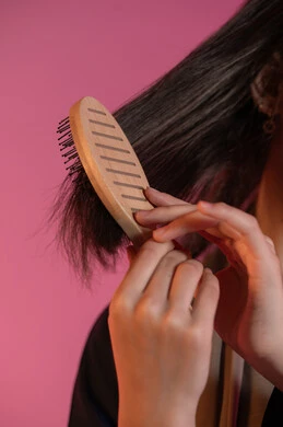 Close-up portrait of an Emirati Gulf Arab woman's hand brushing her hair, the concept of femininity and softness, hair styling and grooming, interest in beauty and elegance, personal hygiene, pink background
