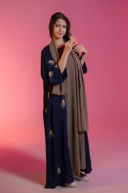 حب التزين والتجمل, المحافظة على شعر صحي وأنيق، مفهوم الاهتمام بالجمال والأناقة والمظهر الخارجي، العناية بالنظافة الشخصية، بورتريه لامرأة عربية خليجية اماراتية مبتسمة ترتدي عباءة زرقاء و تقوم بتمشيط شعرها باستخدام فرشاة الشعر، خلفية وردية