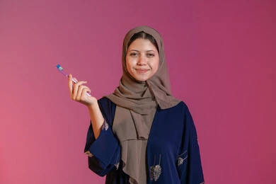 النظر إلى الكاميرا بإيماءات السرور، روتين نظافة الفم اليومية، تجنب التسوس وأمراض اللثة, التأكد من النظافة بعد تناول الطعام, بورتريه لامرأة عربية خليجية اماراتية محجبة ترتدي عباءة زرقاء تمسك بيدها فرشاة الأسنان, خلفية وردية