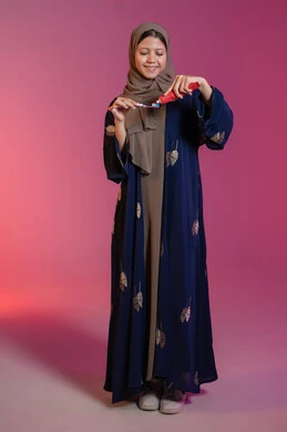 مفهوم العادات الصحية, الحفاظ على الأسنان وتنظيفها بشكل مستمر, ابتسامة ناصعة البياض, روتين نظافة الفم اليومية، تجنب التسوس وأمراض اللثة, بورتريه لامرأة عربية خليجية اماراتية محجبة ترتدي عباءة زرقاء تمسك بيدها الفرشاة, خلفية وردية